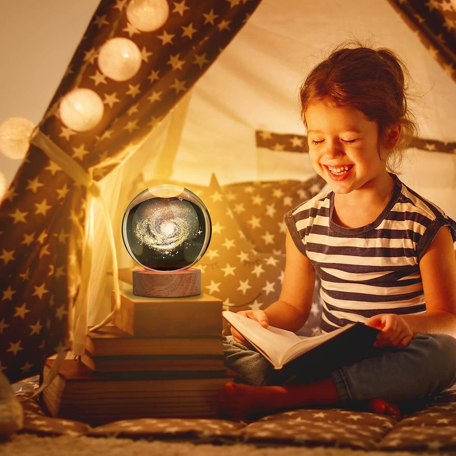 Girl enjoying bedtime story with 3D Galaxy Crystal Ball Night Light in cozy tent setup.