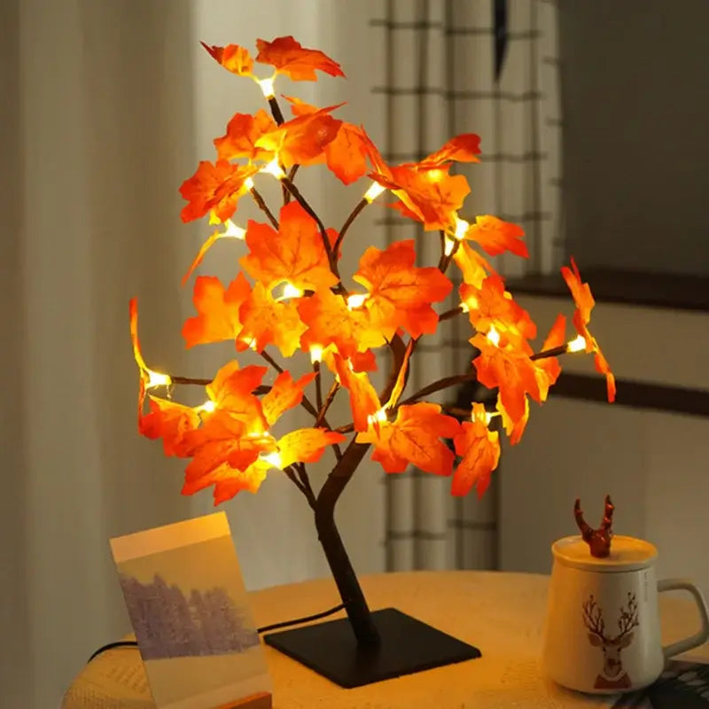 Illuminated Maple Leaf Lamp with vibrant orange LED leaves on a table next to a deer mug and postcard.